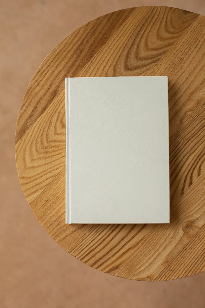 Top view of a simple, blank white book on a round wooden table, ideal for mockup designs.